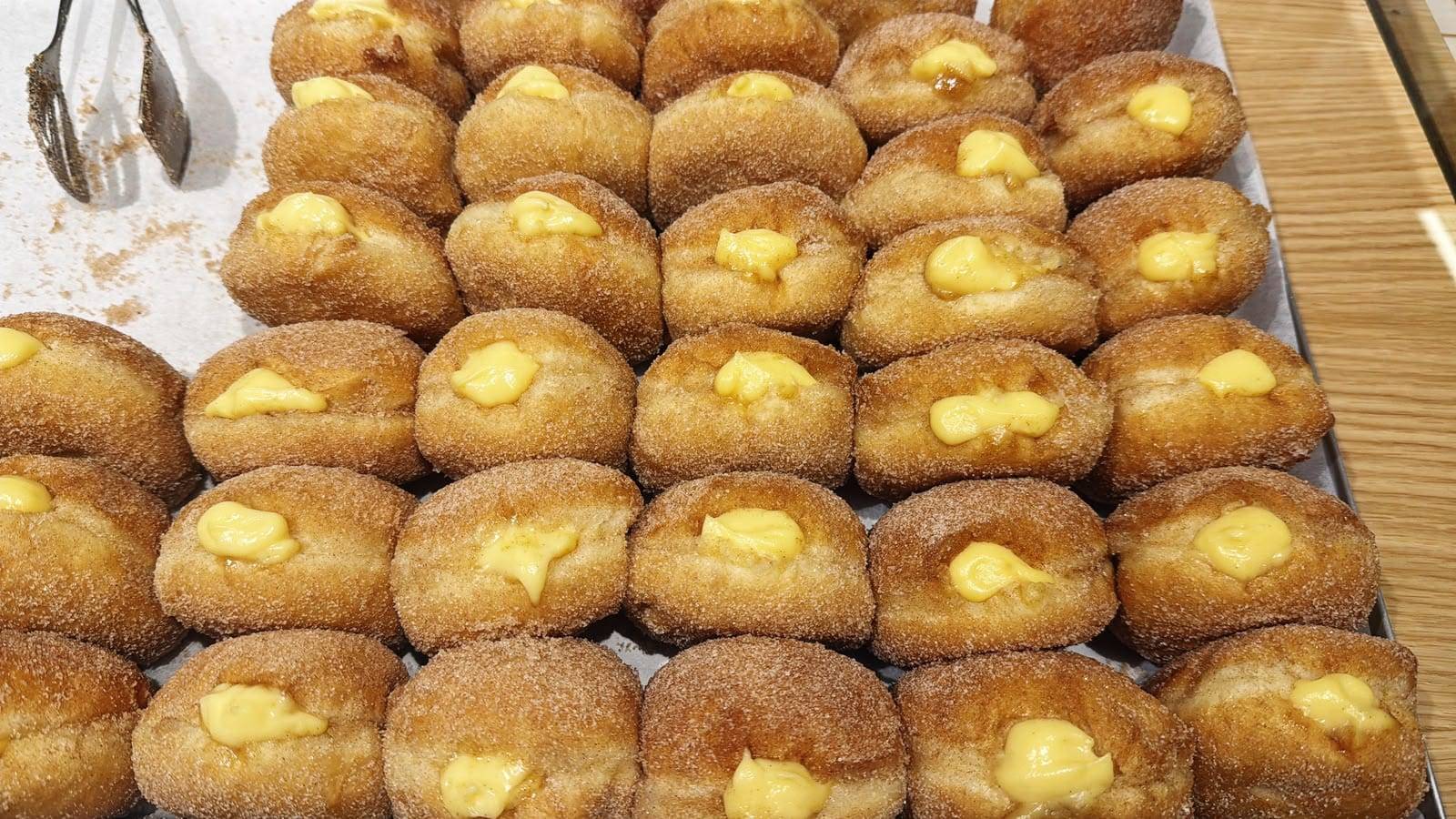Tabuleiro de bolas de Berlim com creme, o creme pasteleiro à vista no topo de cada uma, passadas por açúcar e canela