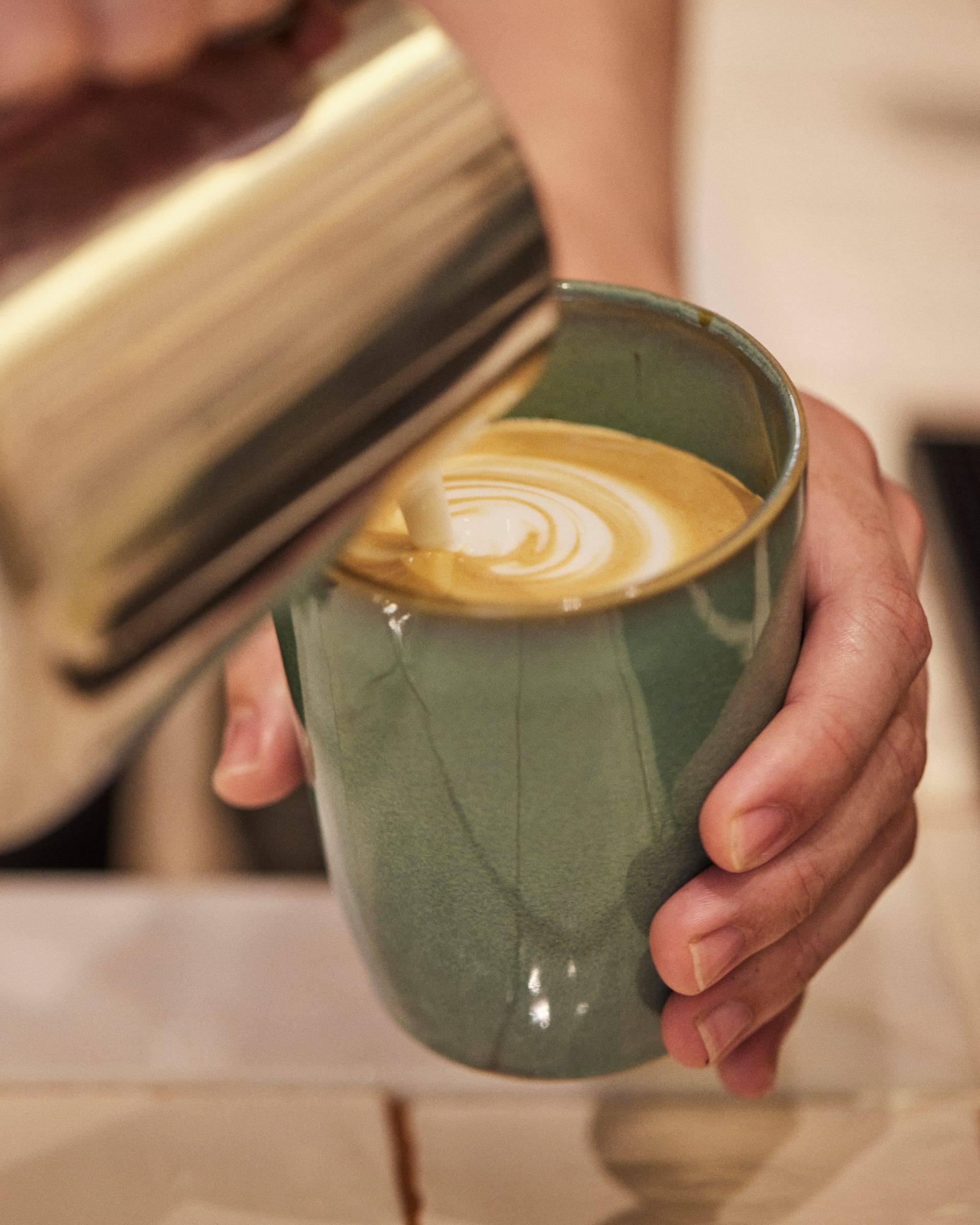 Milk being poured into a cup, forming latte art — hands only in frame