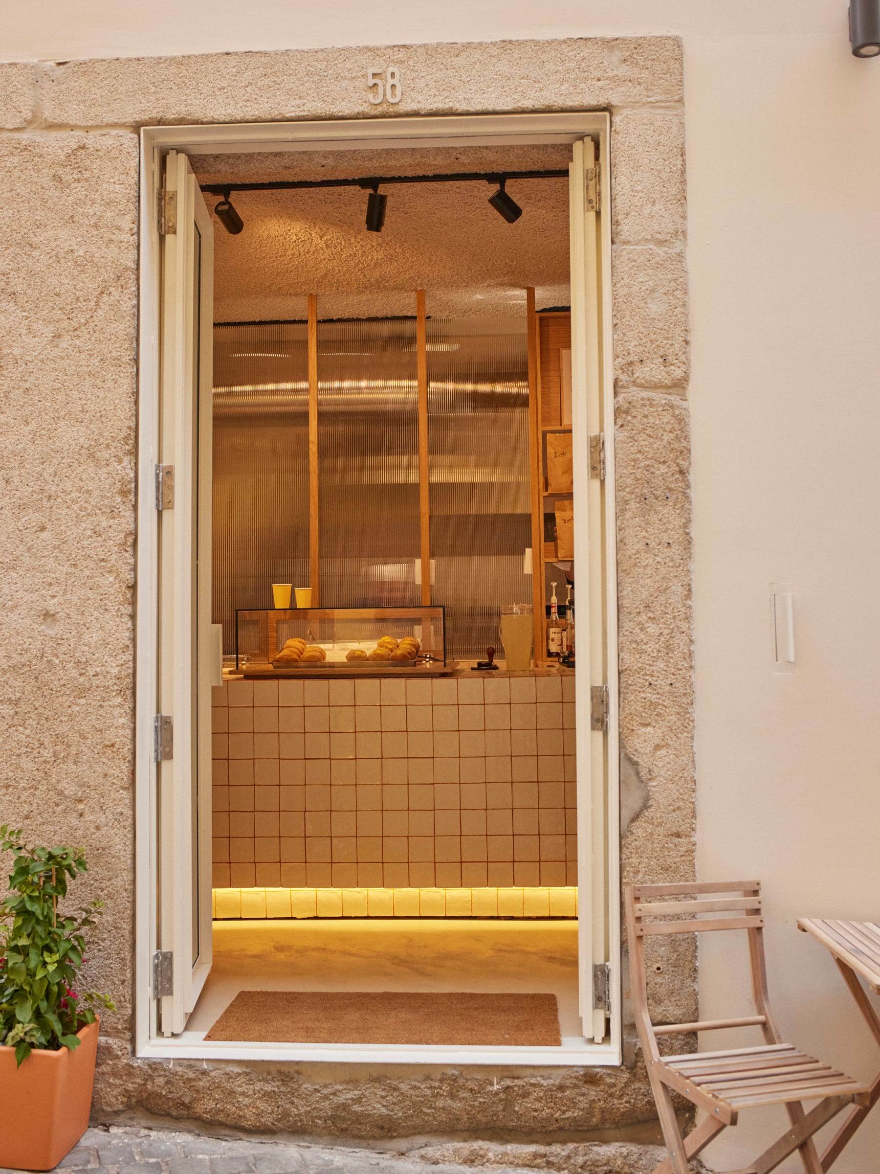 Narrow granite doorway numbered 58, cream folding doors open onto the warmly lit pastry shop, tiled counter glowing at the back