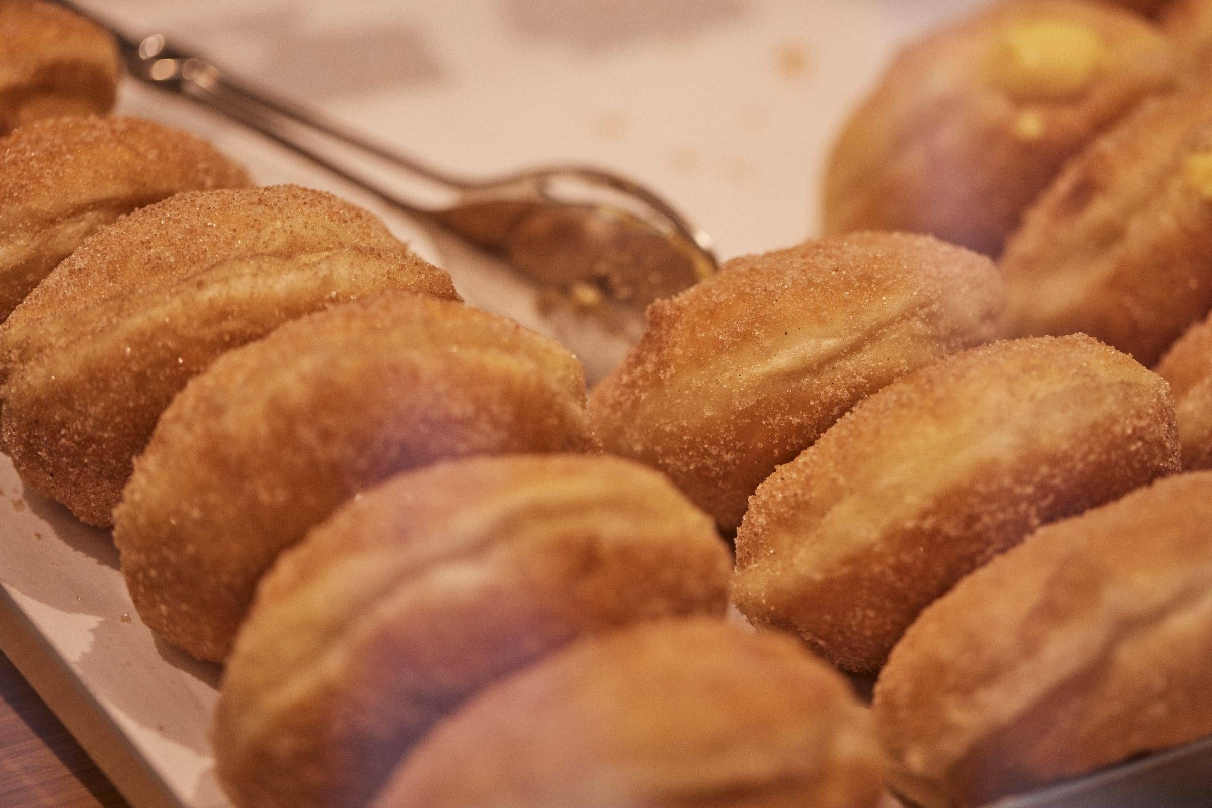 Sugar-rolled bolas de Berlim without cream, in close-up with serving tongs