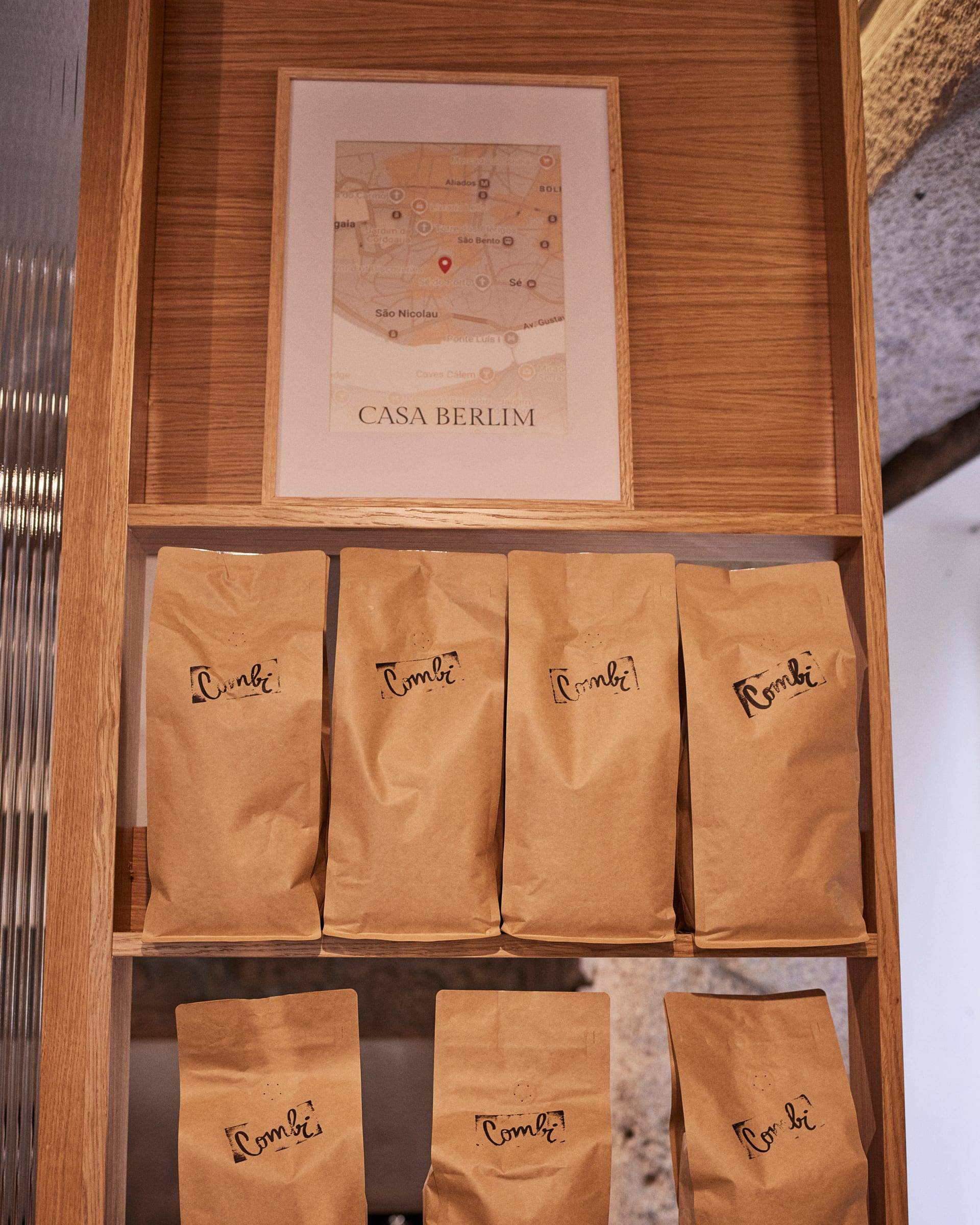Kraft paper coffee bags lined up on an oak shelf, a framed map print on the wall above