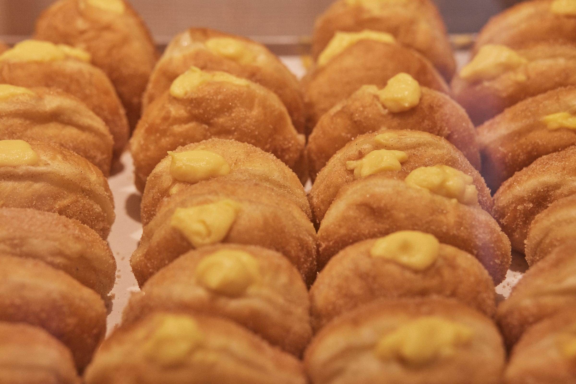 Tabuleiro cheio de bolas de Berlim em grande plano, roladas em açúcar, com creme pasteleiro à vista por cima