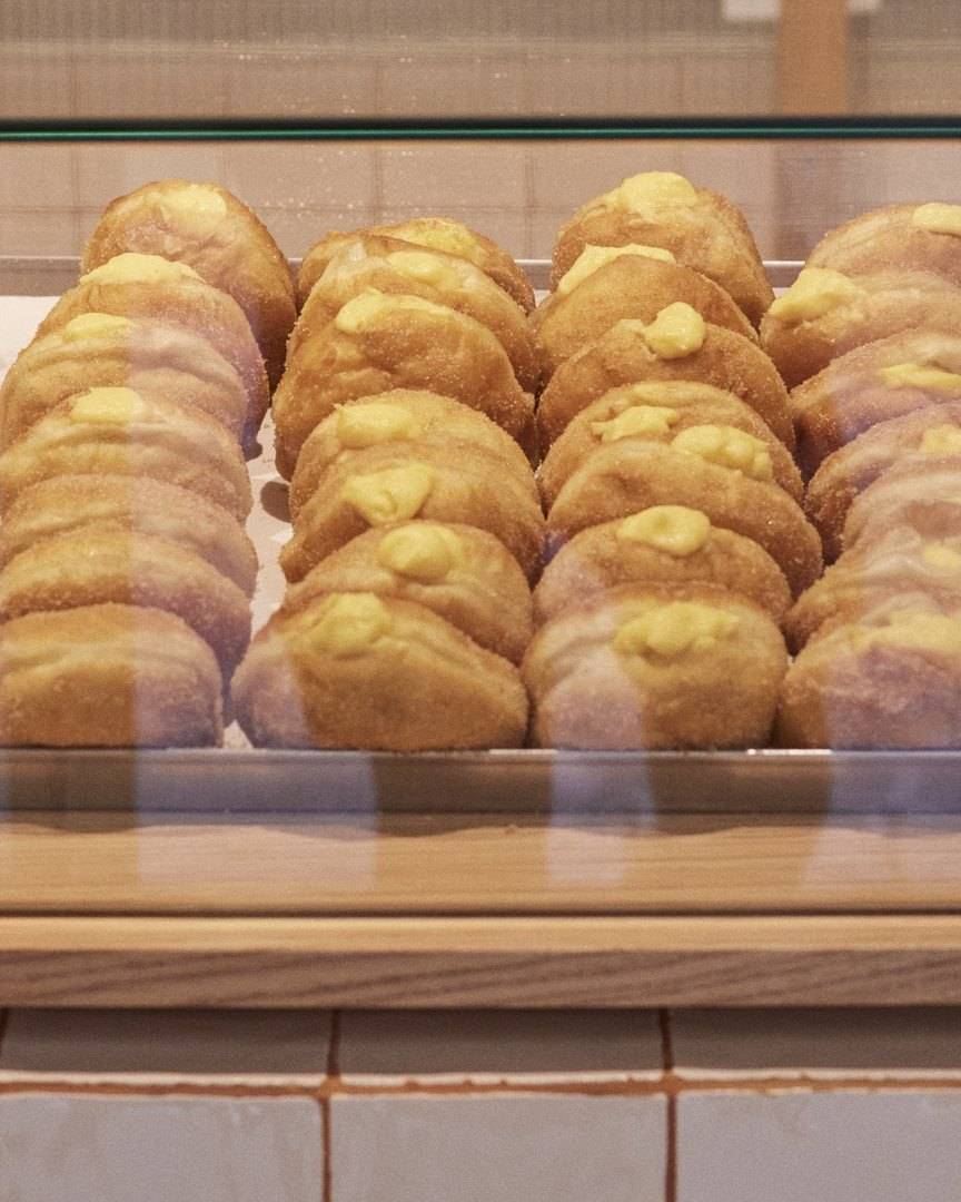 Tabuleiro de bolas de Berlim com creme, acabadas de fazer, na vitrine de vidro do balcão